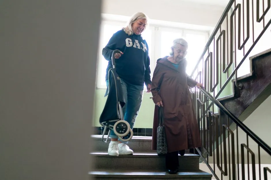 Aidante accompagnant une senior dans un escalier à l'intérieur d'un logement